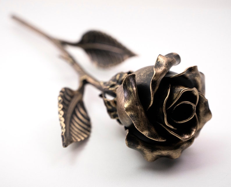 Bronze stained metal rose lays on the white surface. The metal flower is 12 inches long.