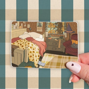 May include: A sticker featuring an illustrated bedroom scene with a bed covered in a pumpkin-themed blanket. A witch's hat sits on a chair. The room has a window with an autumn view.