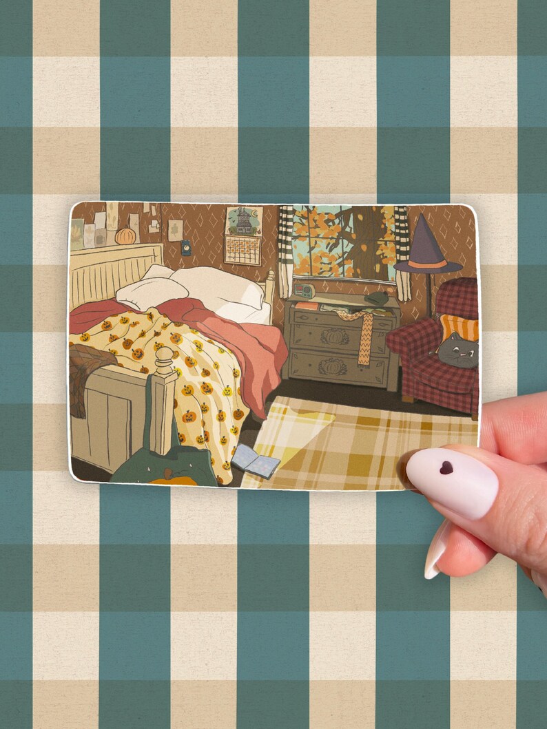 May include: A sticker featuring an illustrated bedroom scene with a bed covered in a pumpkin-themed blanket. A witch's hat sits on a chair. The room has a window with an autumn view.