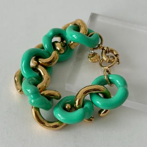 Op de afbeelding: Een opvallende armband met afwisselend goudkleurige en felgroene schakels. De armband heeft een tuimelsluiting en een kleine bedel. De schakels zijn een mix van afgeronde en gebogen vormen, wat een opvallend accessoire creëert.