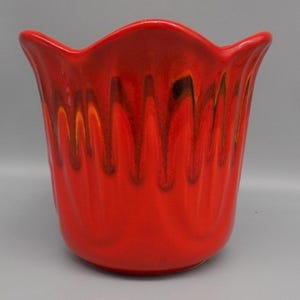 May include: A vibrant red ceramic planter with a wavy rim. The glossy surface features vertical streaks of dark brown and yellow, creating a dripping effect. The planter has a tulip-like shape and a smooth, rounded base.
