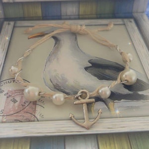 May include: A nautical-themed bracelet with faux pearls and a silver anchor charm. The bracelet is displayed in a decorative box with a seagull illustration and a twine bow.