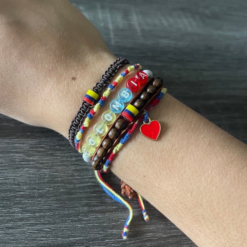 May include: A set of colourful bracelets with a heart charm. The bracelets feature yellow, blue, red and white beads with the word "COLOMBIA" spelled out.