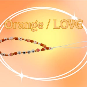 May include: A phone charm featuring orange and white beads, including round beads with the letters L, O, V, E and small heart symbols. The charm includes a white loop attachment and the text Orange / LOVE is displayed above the beaded strand.