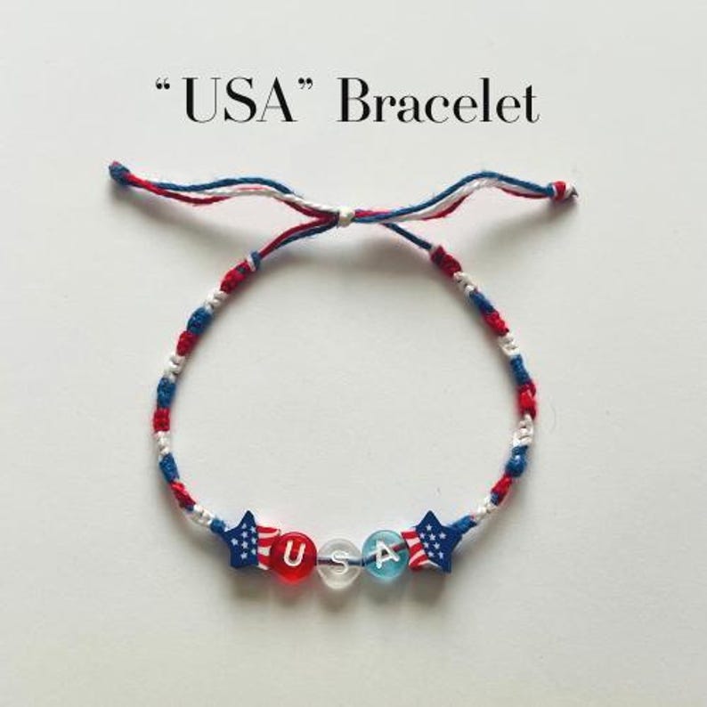 May include: A bracelet featuring red, white, and blue braided cord with two star-shaped beads patterned like the American flag, flanking three round beads spelling out USA in white letters. The text USA Bracelet is printed above the item.