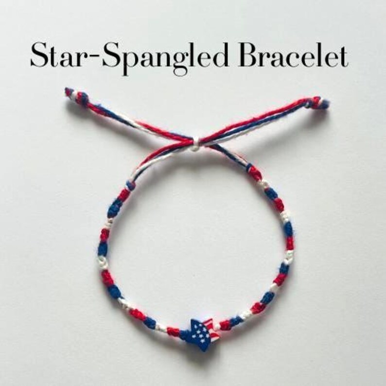 May include: A Star-Spangled Bracelet featuring red, white, and blue braided cord strands. The bracelet includes a central star-shaped charm decorated with a blue field of white stars and red and white stripes, finished with adjustable knotted ends.