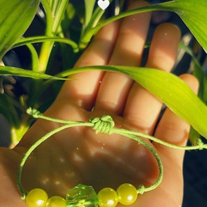 Puede incluir: Un brazalete de cuerda verde con cuatro cuentas verdes y una cuenta verde facetada en el centro.
