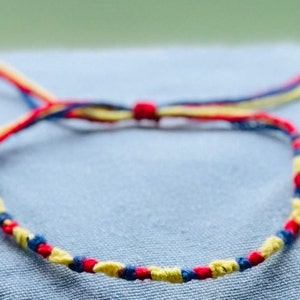 May include: A friendship bracelet made with red, yellow and blue string. The bracelet is tied in a knot and is ready to be worn.