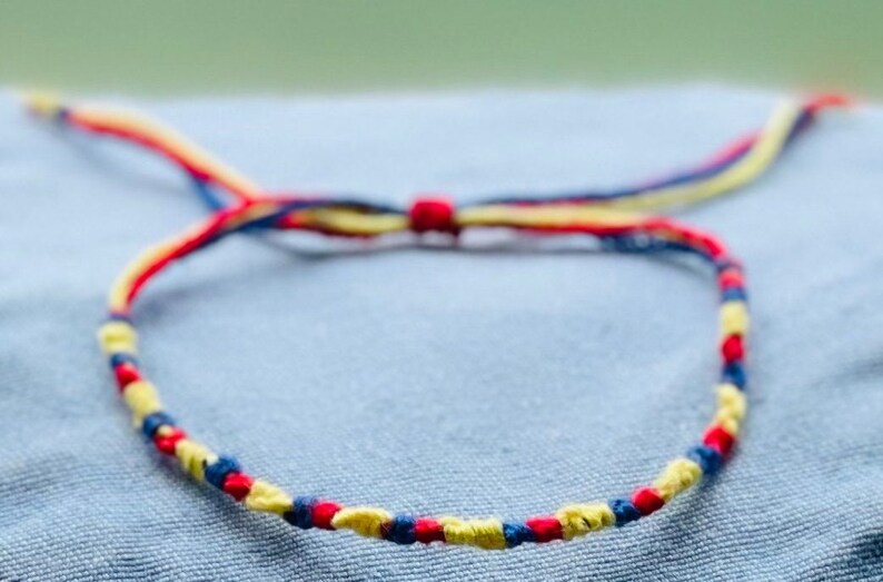 May include: A friendship bracelet made with red, yellow and blue string. The bracelet is tied in a knot and is ready to be worn.