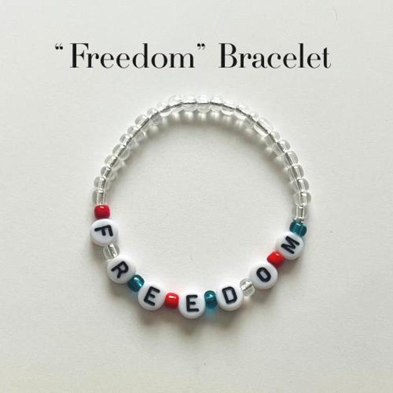 May include: A circular beaded bracelet featuring the word Freedom spelt out with white alphabet beads with black lettering. The design includes clear, red, and teal accent beads interspersed throughout the strand. The text Freedom Bracelet is visible.