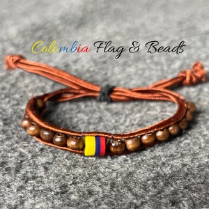 May include: A brown cord bracelet with wooden beads and a small yellow, blue and red bead representing the Colombian flag. The bracelet is tied with a knot and has a tassel.