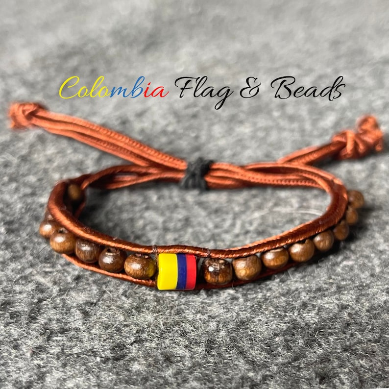 May include: A brown cord bracelet with wooden beads and a small yellow, blue and red bead representing the Colombian flag. The bracelet is tied with a knot and has a tassel.