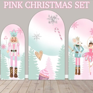 May include: Pink Christmas themed party decorations with a nutcracker, a mouse, a ballerina, and a cupcake. The decorations are in the shape of arches and are printed with snowflakes, candy canes, and hearts.