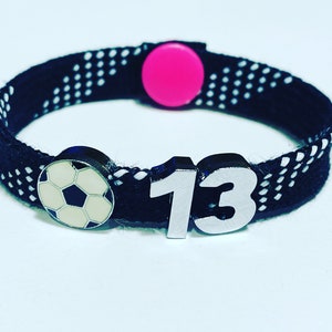 May include: Black and white patterned bracelet with a pink adjustable clasp, a silver football charm, and a silver charm with the number 13.
