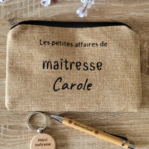 May include: A brown burlap zippered pouch with the text "Les petites affaires de maitresse Carole" on the front. A wooden keychain with the text "Merci maitresse Carole" and a wooden pen with the text "Maitresse Carole" are also included.