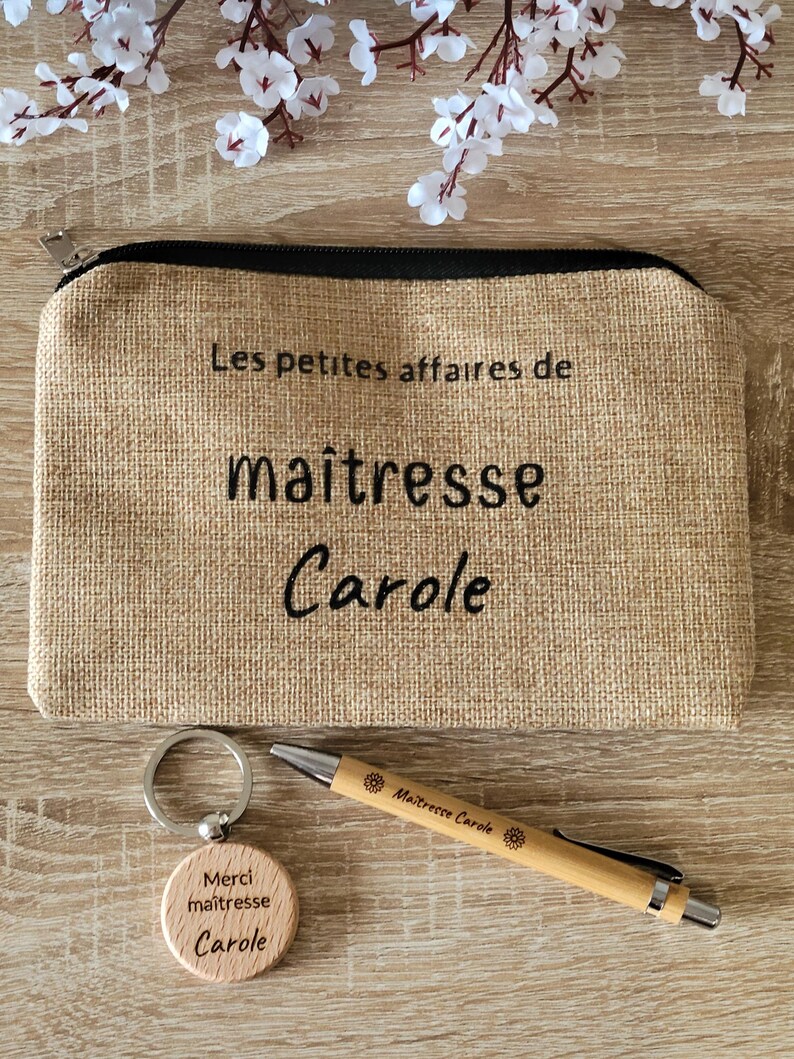 May include: A brown burlap zippered pouch with the text "Les petites affaires de maitresse Carole" on the front. A wooden keychain with the text "Merci maitresse Carole" and a wooden pen with the text "Maitresse Carole" are also included.