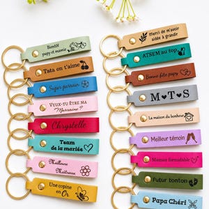 May include: A collection of colorful leather keychains with gold-tone rings. Each keychain features engraved text and small illustrations. The keychains are in various colors, including pink, blue, green, and yellow.