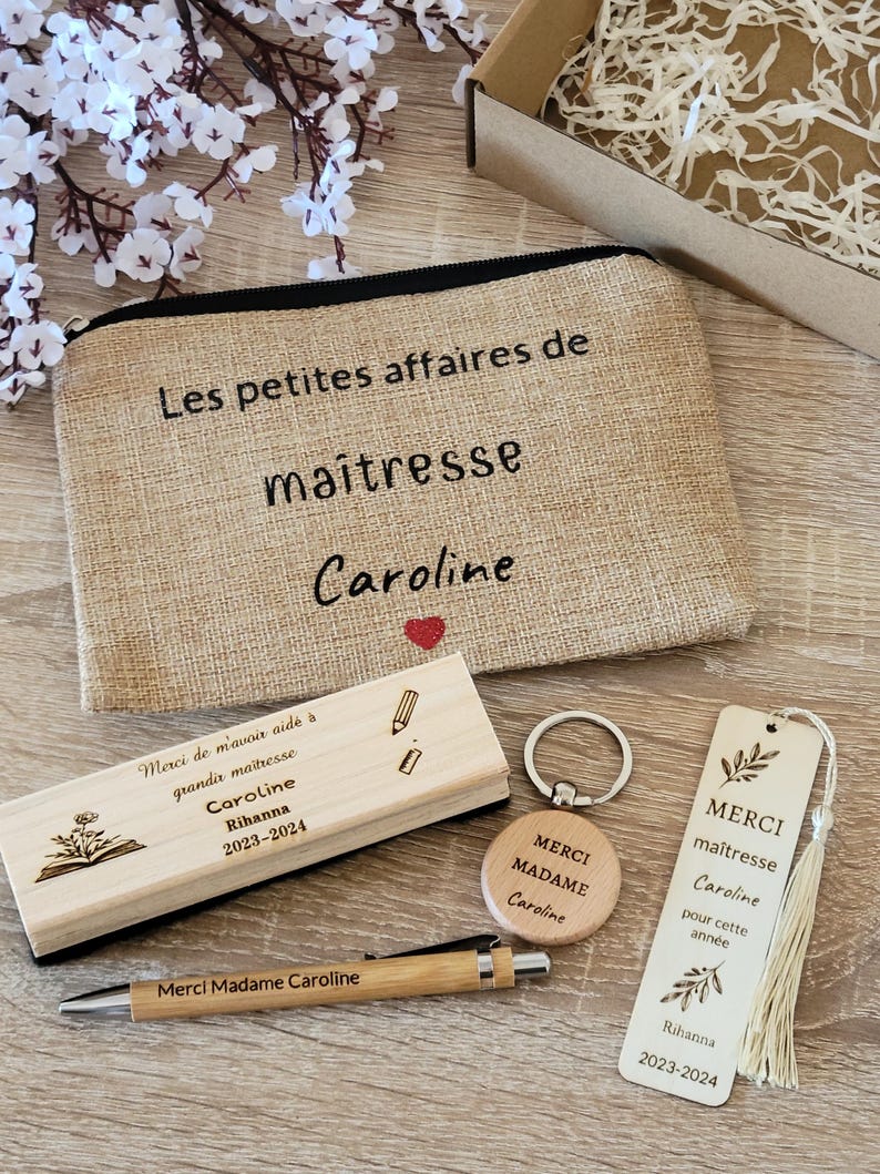 May include: A teacher appreciation gift set with a burlap makeup bag that says "Les petites affaires de maitresse Caroline", a wooden pencil holder with the text "Merci de m'avoir aid&eacute; &agrave; grandir maitresse Caroline Rihanna 2023-2024", a wooden keychain with the text "Merci Madame Caroline", a wooden bookmark with the text "Merci maitresse Caroline pour cette ann&eacute;e Rihanna 2023-2024", and a pen.