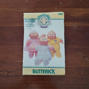 May include: A Butterick 3269 sewing pattern envelope for Cabbage Patch Kids Preemie clothes. The front features three dolls wearing a pink dress, a yellow outfit, and a white patterned sleeper. The text includes Cabbage Patch Kids Preemie.