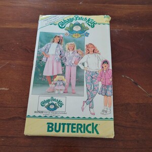 Könnte beinhalten: Ein Butterick-Schnittmusterumschlag für Cabbage Patch Kids-Kleidung. Das Cover zeigt Illustrationen von Kindern und Puppen in verschiedenen Outfits, darunter ein rosa Rock, eine geblümte Hose und eine rosa Kapuzenjacke. Text beinhaltet Cabbage Patch Kids.