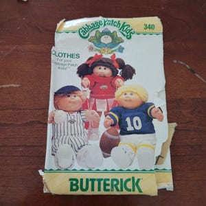 Puede incluir: Un sobre de patrón de costura Butterick para ropa de muñecos Cabbage Patch Kids, número 340. El frente presenta ilustraciones de tres muñecos con trajes deportivos: un uniforme de béisbol, un traje de animadora y una camiseta de fútbol americano con el número 10.
