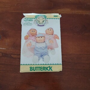 May include: A Butterick sewing pattern envelope numbered 6981 for Cabbage Patch Kids Preemie clothes. The front features illustrations of three dolls wearing various outfits including a pink hooded sleeper, a blue striped romper, and a pink dress.