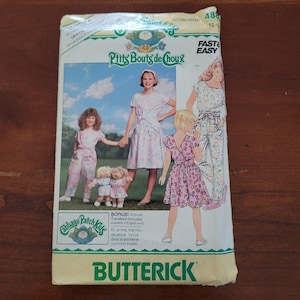 May include: A Butterick sewing pattern envelope for Cabbage Patch Kids clothing, featuring illustrations of children wearing a dress and jumpsuit with floral patterns. The package includes text for a bonus iron-on transfer and pattern number 4882.