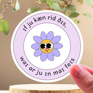 May include: Purple and white round sticker with a cartoon flower with a yellow face and big eyes. The text on the sticker reads "if you can read this, wai ar ju in maifeis".
