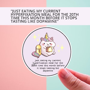May include: A round sticker with a purple background features a cartoon unicorn eating a sandwich. The sticker has the text "just eating my current hyperfixation meal for the 20th time this month before it stops tasting like dopamine".