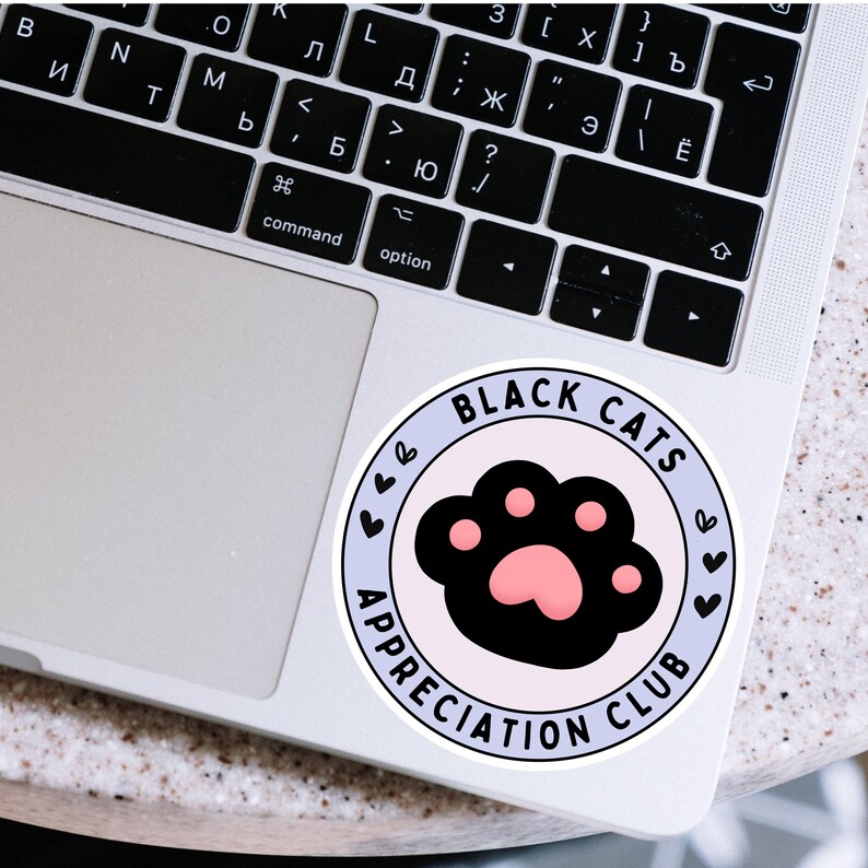May include: A round sticker with the text "BLACK CATS APPRECIATION CLUB" in a light blue circle. The sticker features a black cat paw print with a pink paw pad, and small heart designs.