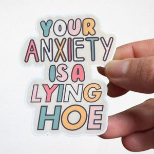 Może przedstawiać: Kolorowa naklejka z napisem "YOUR ANXIETY IS A LYING HOE" w r&oacute;żnych pastelowych kolorach. Naklejka ma białą obw&oacute;dkę i jest trzymana w dłoni.