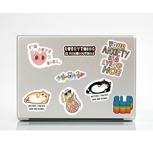 Może przedstawiać: Laptop pokryty kolorowymi naklejkami. Projekty obejmują r&oacute;żowe serce, kota, żabę na kuli dyskotekowej i frazy takie jak "Everything is Figureoutable" i "Your Anxiety is a Lying Hoe."