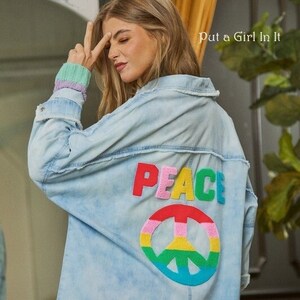 May include: A light blue denim jacket with a rainbow peace sign and the word "PEACE" in colorful letters on the back.