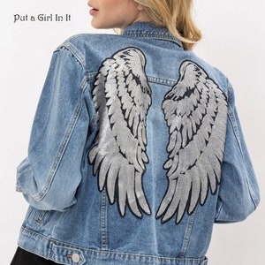 May include: A light blue denim jacket with silver sequin angel wings on the back. The text "Put a Girl In It" is visible in the top left corner of the image.