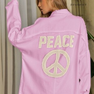 May include: A light pink denim jacket with a white peace sign and the word "PEACE" embroidered on the back.