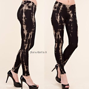 May include: Black leggings with a tie-dye pattern in shades of beige and white. The leggings are form-fitting and have a high waist. The text "Put a Girl In It" is visible on the lower left side of the image. The model is wearing black high heels.