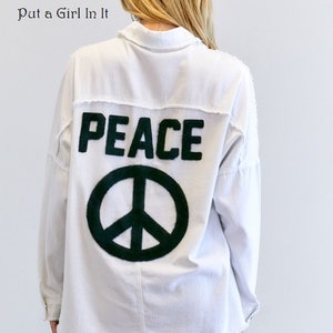 May include: White long-sleeved shirt with a black peace sign and the word "PEACE" in black lettering on the back.