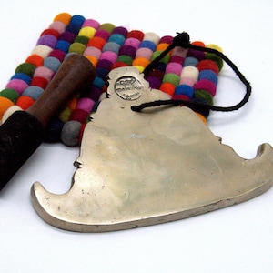 May include: A silver-colored metal object with a curved edge and a black cord, a wooden mallet, and a colorful felt ball mat. The mat has various colors, including red, blue, and yellow.