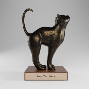 Puede incluir: Una escultura de gato color bronce con acabado texturizado, sobre una base rectangular de madera. El gato se muestra con la cola arqueada hacia arriba y la cabeza inclinada hacia atrás. La parte frontal de la base de madera tiene una placa clara con el texto "Your Text Here" impreso en una fuente oscura sin remates.