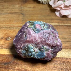 May include: A rough, pink and blue crystal with a natural, irregular shape. The crystal has a mix of pink, blue, and green hues.