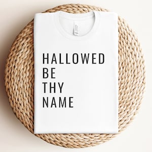 May include: White t-shirt with black text that reads "HALLOWED BE THY NAME".