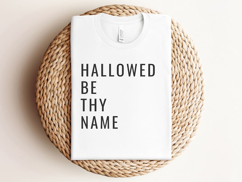 May include: White t-shirt with black text that reads "HALLOWED BE THY NAME".