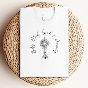 May include: White t-shirt featuring a black and white illustration of a monstrance and the text "Body, Blood, Soul & Divinity".