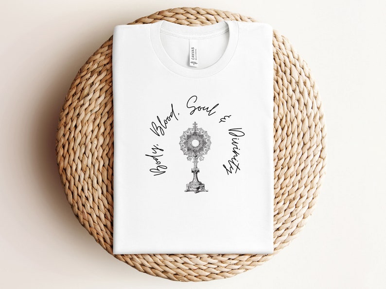 May include: White t-shirt featuring a black and white illustration of a monstrance and the text "Body, Blood, Soul & Divinity".
