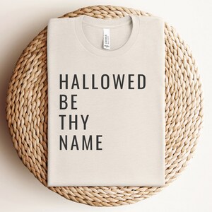 May include: A beige t-shirt with the text "HALLOWED BE THY NAME" printed in black.