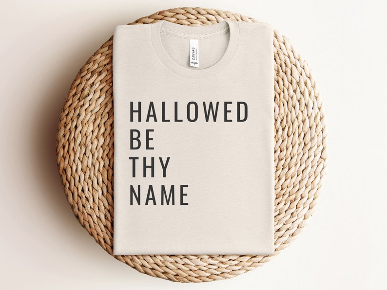 May include: A beige t-shirt with the text "HALLOWED BE THY NAME" printed in black.