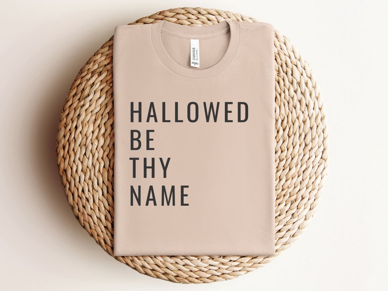 May include: A light brown t-shirt with the text "HALLOWED BE THY NAME" printed in black.