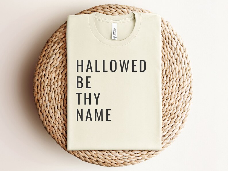 May include: A light beige t-shirt with the text "HALLOWED BE THY NAME" printed in black.