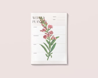 May include: A weekly planner with a floral design featuring pink flowers and green leaves. The planner has sections for each day of the week, Monday through Sunday, with space for writing tasks and notes.