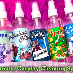 May include: Five clear spray bottles with white tops, each labeled with a different cartoon character and flavor. The labels read "Grape", "Feeling Chippy", "Epic Woods", "That New", and "Stontus Blue". The text "Fursuit/Cosplay Cleaning Spray" is at the bottom.